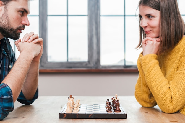 Free photo close-up of young couple with their hand clasped looking at each other playing chess