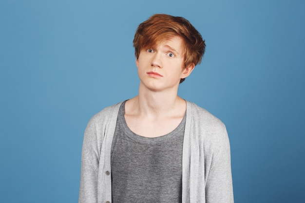 Free photo close up of young good-looking happy red-haired guy in gray t-shirt under cardigan  with confused expression, after receiving hard question on exam in university.