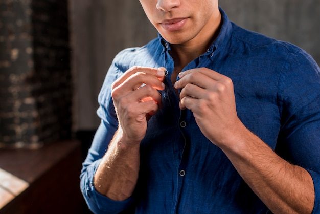 Close-up of a young man buttons up his blue shirt