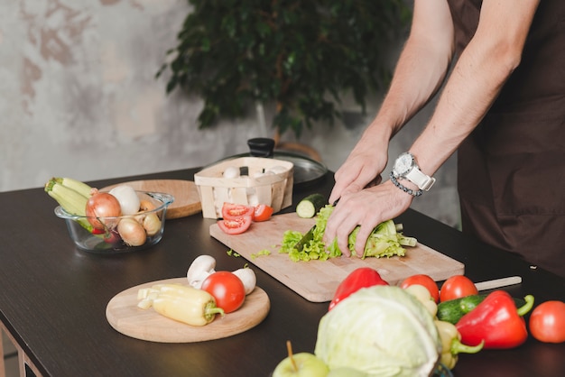 Close-up of young man cutting lettuce with knife on chopping board