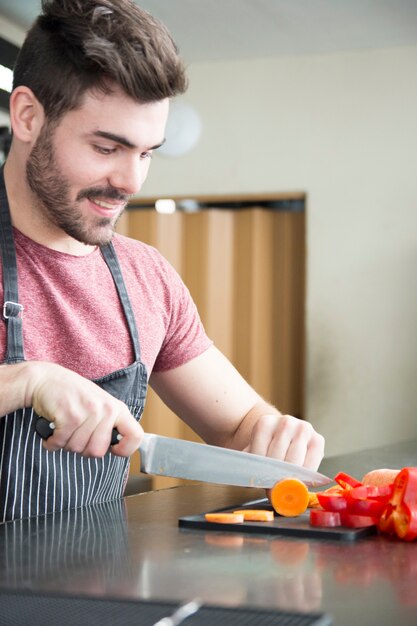 Close-up of young man cutting slices of carrot with sharp knife