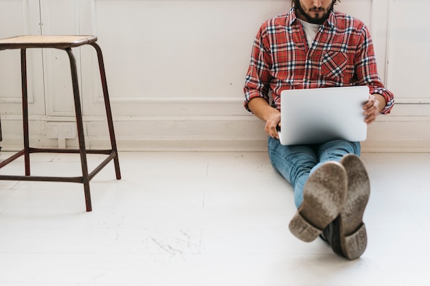 Free photo close-up of a young man sitting on floor with crossed legs using laptop