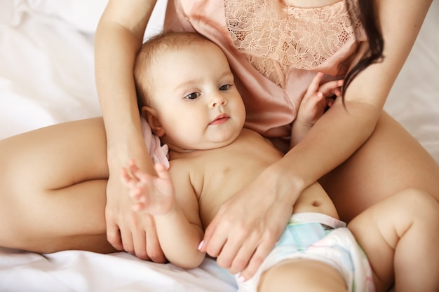 Close up of young mother in sleepwear and her newborn baby lying on bed in morning.