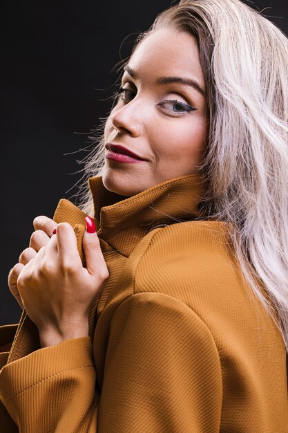 Close-up of young woman holding yellow jacket and posing against black background