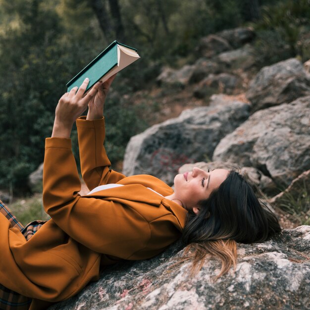 Close-up of a young woman leaning on rock reading the book