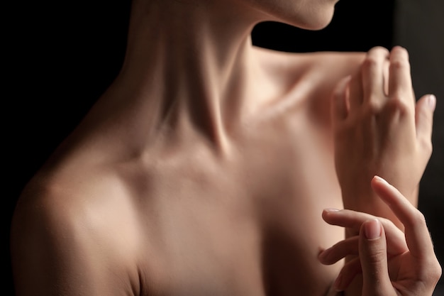 Free photo the close-up of a young woman's neck and hands  on dark background