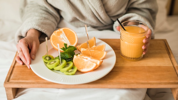 Free photo close-up of young woman with plate of fruits and an orange juice on wooden tray