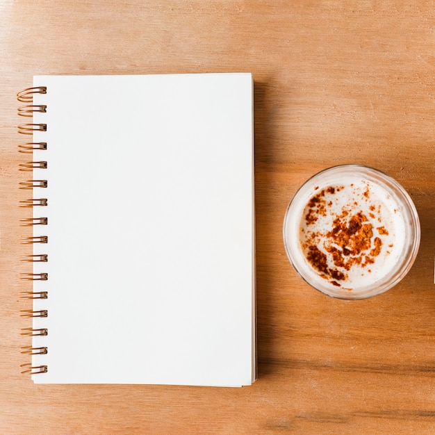 Free photo closed white spiral notebook and coffee glass with cocoa powder