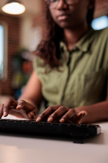 Free photo closeup of african american woman programmer writing code on computer keyboard while working remote from home living room. selective focus on hands typing and coding software on pc.