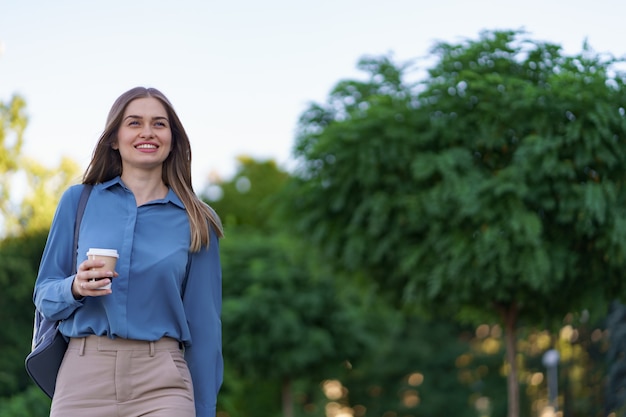 Closeup attractive woman in motion with takeaway coffee on city street. Portrait blonde girl holding paper cup with hot drink outdoor.