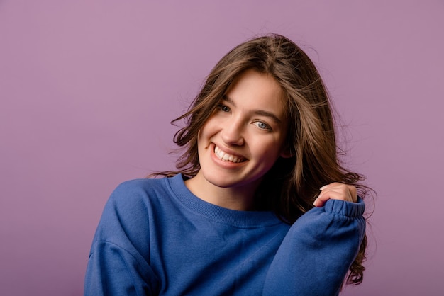 Free photo closeup of attractive young caucasian brunette woman in sweatshirt smiles broadly with teeth on purple background beauty emotions people concept