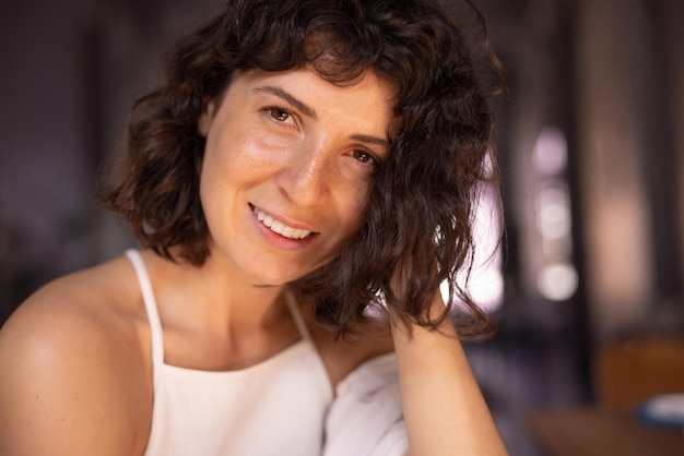 Closeup of attractive young caucasian girl with dark short hair in white top looks at camera indoors