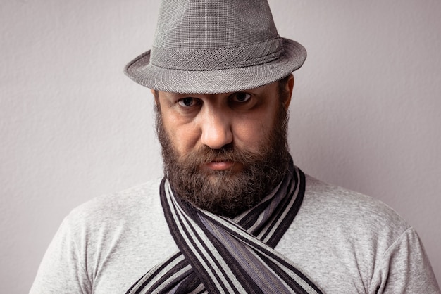 Free photo closeup of a bearded man wearing a light grey t-shirt, hat and scarf on a grey background