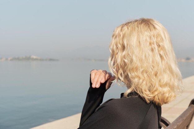 Closeup on a beautiful adult blonde woman sitting on a bench and looking at the sea and blue sky silhouette of a woman space for text idea for background