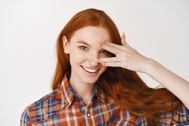 Free Photo closeup of beautiful redhead lady with blue eyes and pale skin smiling at camera standing over white background