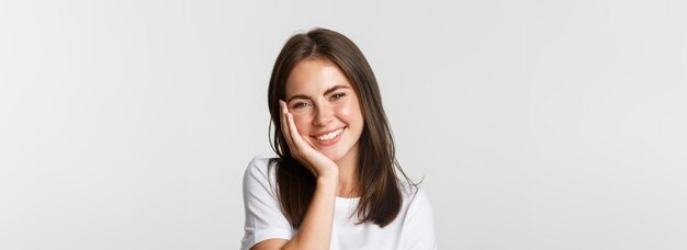 Closeup of beautiful smiling brunette girl touching cheeks blushing over white background