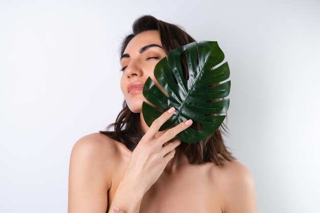 Closeup beauty portrait of a topless woman with perfect skin and natural makeup with monstera palm leaf