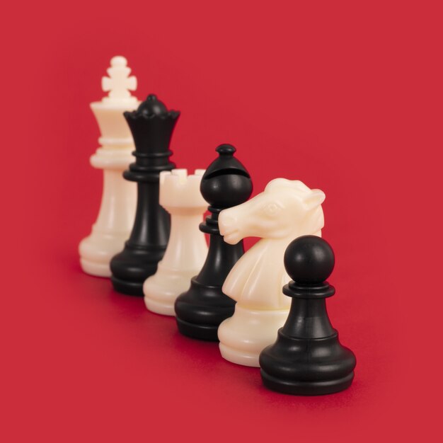 Closeup of black and white chess pieces lined up on a bright red