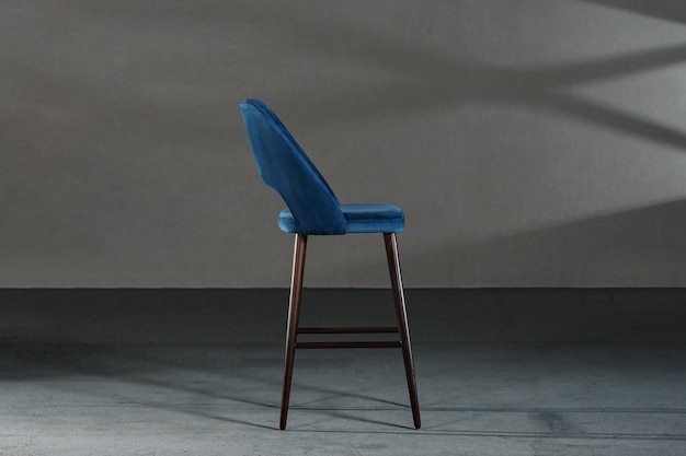 Closeup of a blue chair with high legs in a room with gray walls