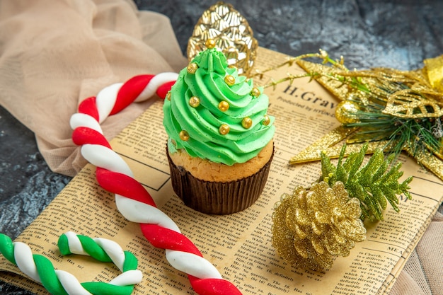 Closeup bottom view mini cupcake xmas candies xmas ornaments on newspaper beige shawl on dark background