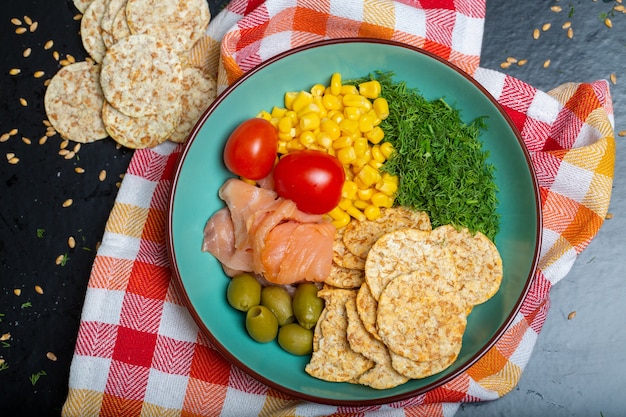 Free Photo closeup of a bowl of salad with salmon, crackers and vegetables on a napkin on the table