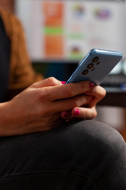 Closeup of businesswoman hand chatting with friend using modern smartphone while working in startup company office. Executive manager browsing on social media, searching business app