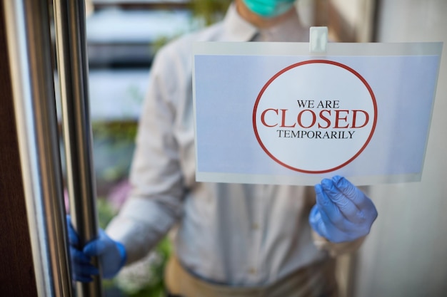 Free photo closeup of cafe owner handing closed sign at the door due to coronavirus epidemic