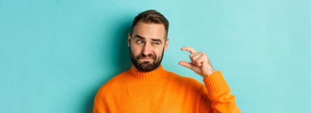 Free photo closeup of caucasian man showing small or little with fingers standing disappointed over light blue