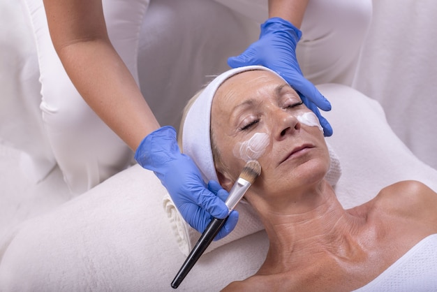 Free photo closeup of a caucasian senior woman applying face cream in a beauty salon