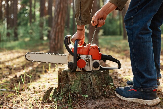 Closeup of chainsaw on wooden stump, faceless woodsman start saw