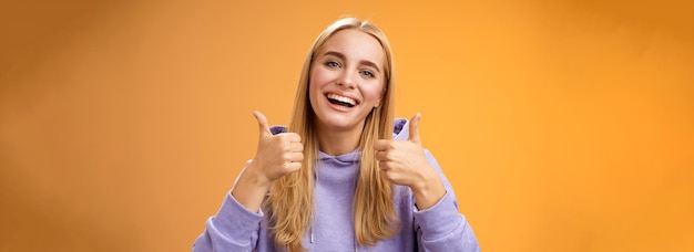 Free photo closeup charming delighted cute female customer give positive feedback show thumbsup like gesture smiling broadly agree recommend perfect product skincare standing satisfied orange background