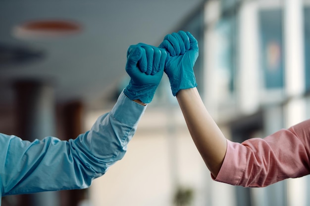 Closeup of colleagues fist bumping while wearing protective gloves