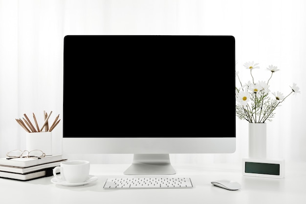 Closeup of a computer, a cup of coffee, a vase of flowers, and more on a white desk, indoors