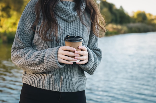 Free photo closeup a cup of coffee in the hands of a woman in nature near the river