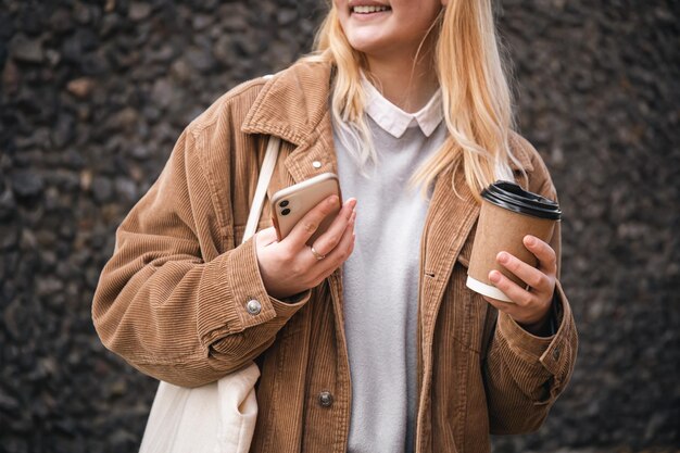 Closeup a cup of coffee and a smartphone in female hands in the city