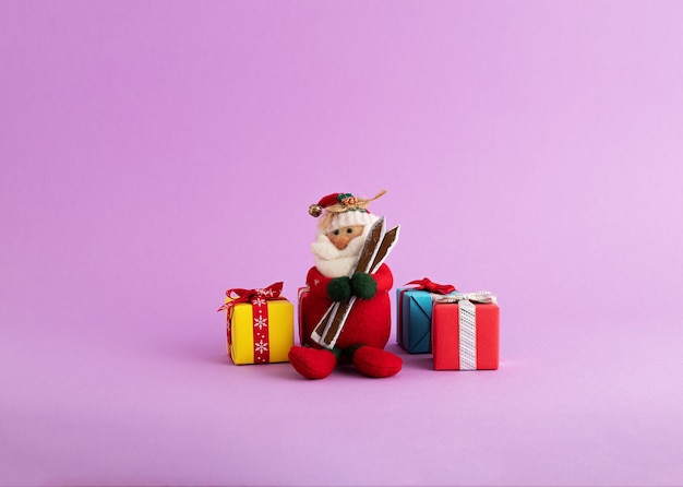 Free photo closeup of a cute santa claus toy and colorful gift boxes in the purple background