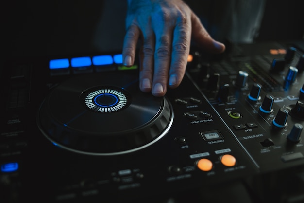 Closeup of a DJ working under the colorful lights in a studio with a blurry