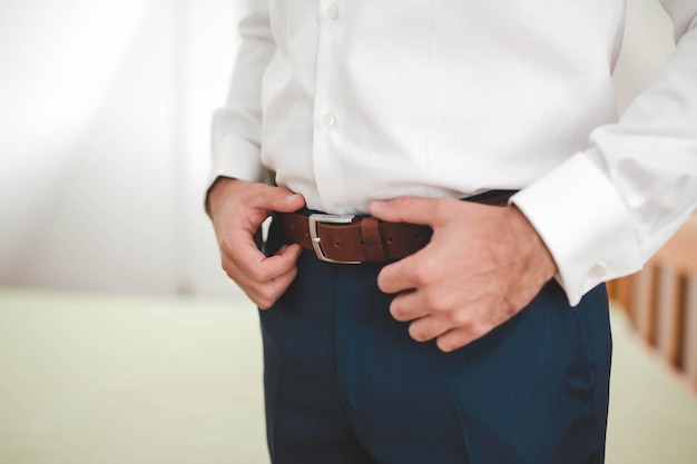 Closeup of an elegant  man standing with his hands on his leather belt on the trousers