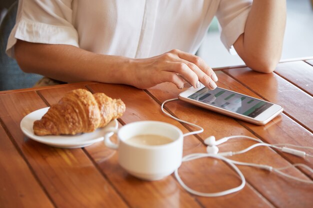 Closeup of female hands texting a message on the smartphone while having morning coffee