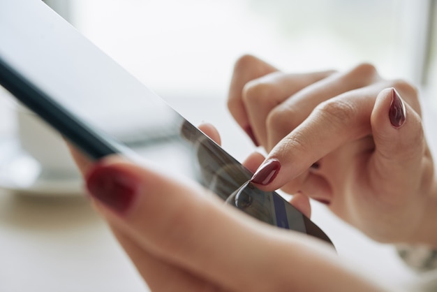 Closeup of female hands with dark red nail manicure using smartphone