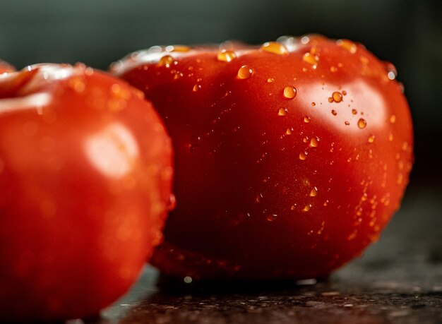 Closeup of fresh ripe tomatoes with water droplets on a black granite kitchen counter surface