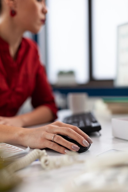 Closeup of hand using wireless computer mouse in startup office. Entrepreneur fingers with ring cliking at desk. Manager in red shirt scrolling content on desktop computer in company worskpace.