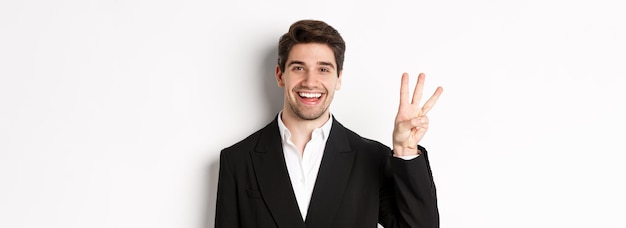 Free photo closeup of handsome businessman in black suit smiling amazed showing number three standing over whit