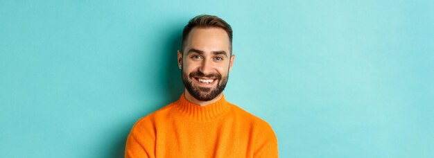 Closeup of handsome caucasian man smiling at camera looking confident wearing orange sweater standin