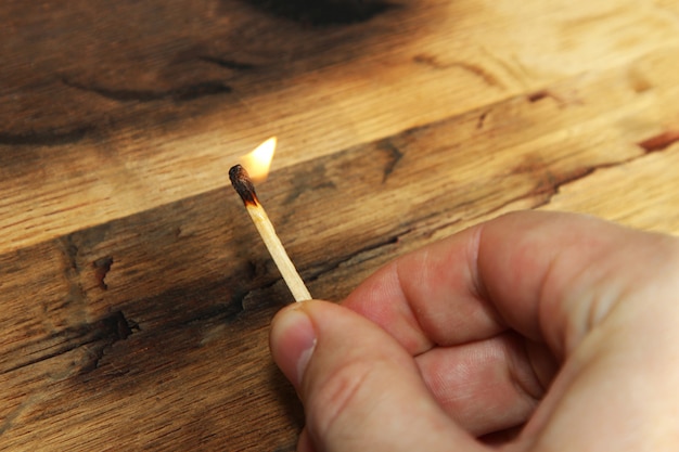 Free Photo closeup high angle shot of a person holding a burning matchstick over a wooden surface