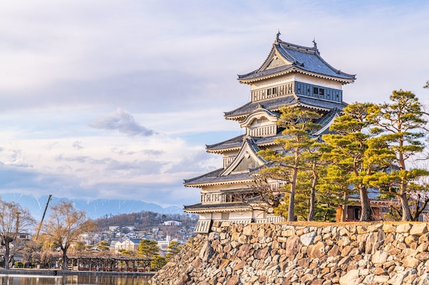 Closeup of the historic Matsumoto Castle with a stone wall and beautiful trees on a cloudy day