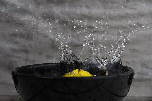 Closeup of a lemon and splashing water in a black bowl under the lights against a grey wall