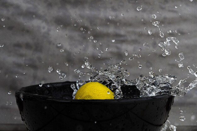 Closeup of a lemon and splashing water in a black bowl under the lights against a grey wall