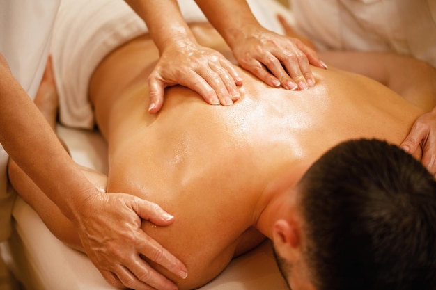 Closeup of man having back massage by two therapists at the spa