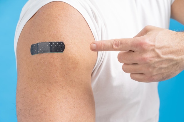 Free Photo closeup a man pointing finger on his shoulder with a band aid on it after receiving the covid19 vaccine vaccine against covid19 or coronavirus aging male skin fair skin men healthcare concept